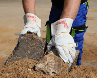 Weiße Leder Arbeitshandschuhe halten Steine in der Hand die im Sand sind